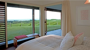 Une chambre à coucher avec un grand lit, un banc et une vue sur un paysage verdoyant, visible à travers des portes ouvertes.