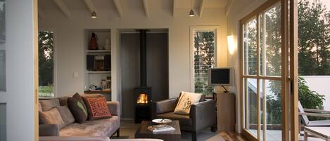 A modern living room with a fireplace, comfortable seating, and large windows offering a view of the outdoors.