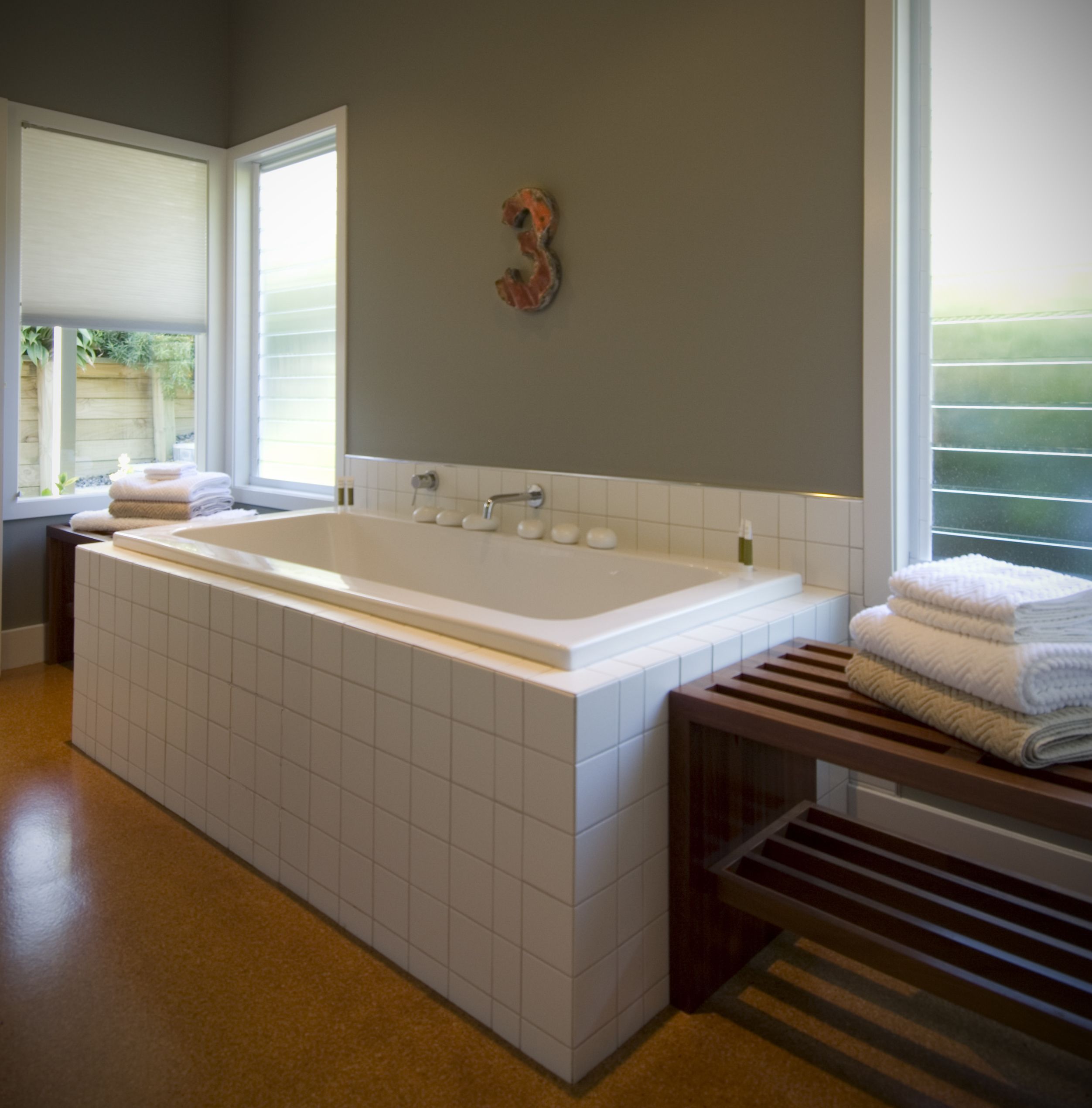 A modern bathroom with a large bathtub, a wooden bench, and a towel rack.
