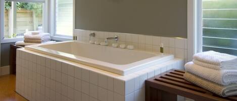 A modern bathroom with a large bathtub, a wooden bench, and a towel rack.