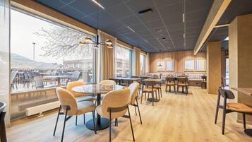 Et moderne spiseområde med runde borde og stole, store vinduer med udsigt og et træloft.