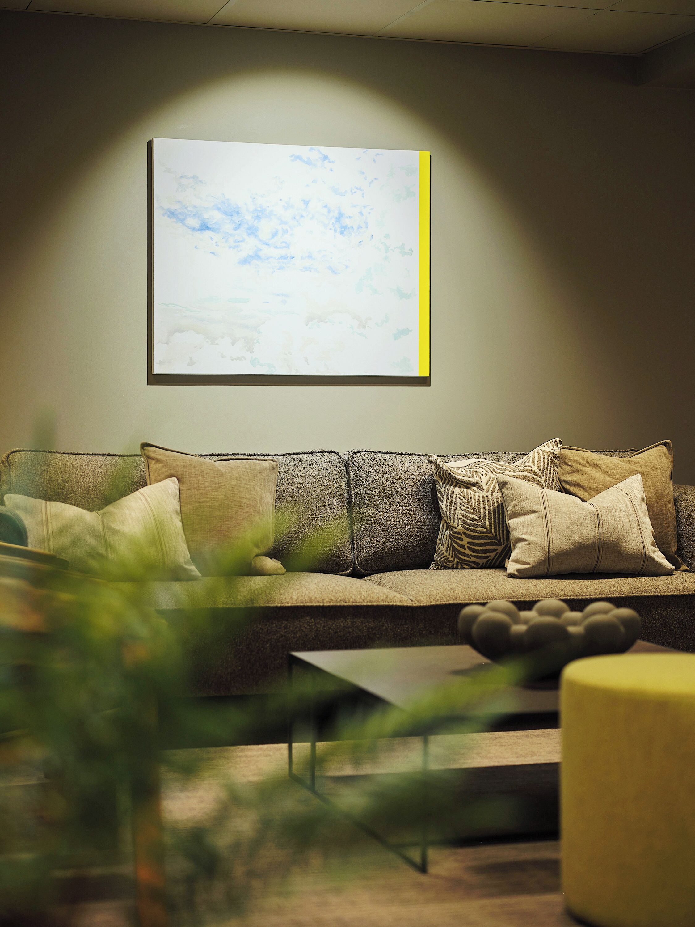 A modern living room with a sofa, cushions, a coffee table, and a framed picture on the wall.