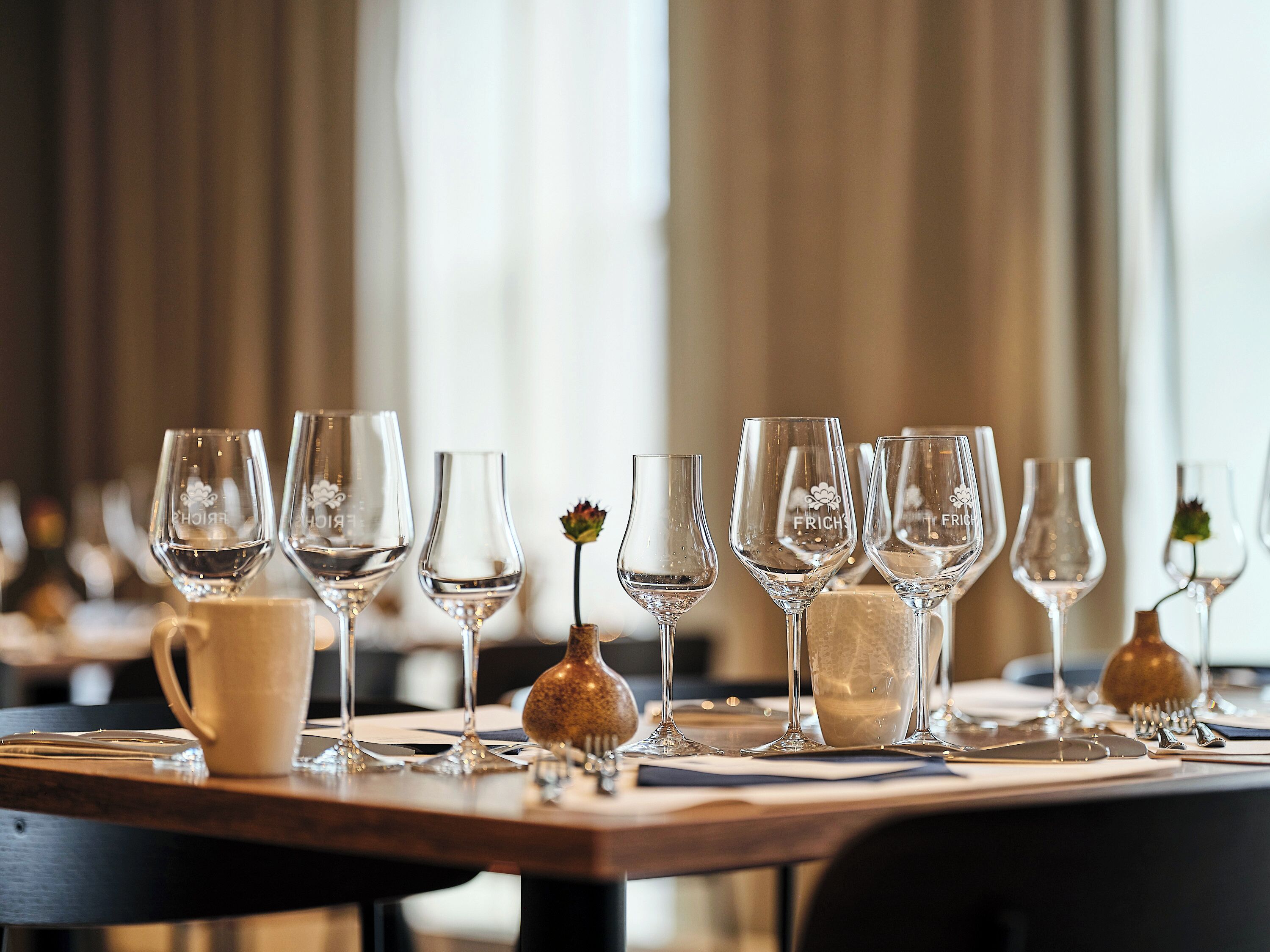 A dining table set with multiple wine glasses and a pitcher, with a blurred background suggesting a restaurant setting.