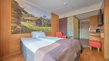 Una habitación de hotel con una cama, una silla, una mesita y un cuadro de un paisaje montañoso.