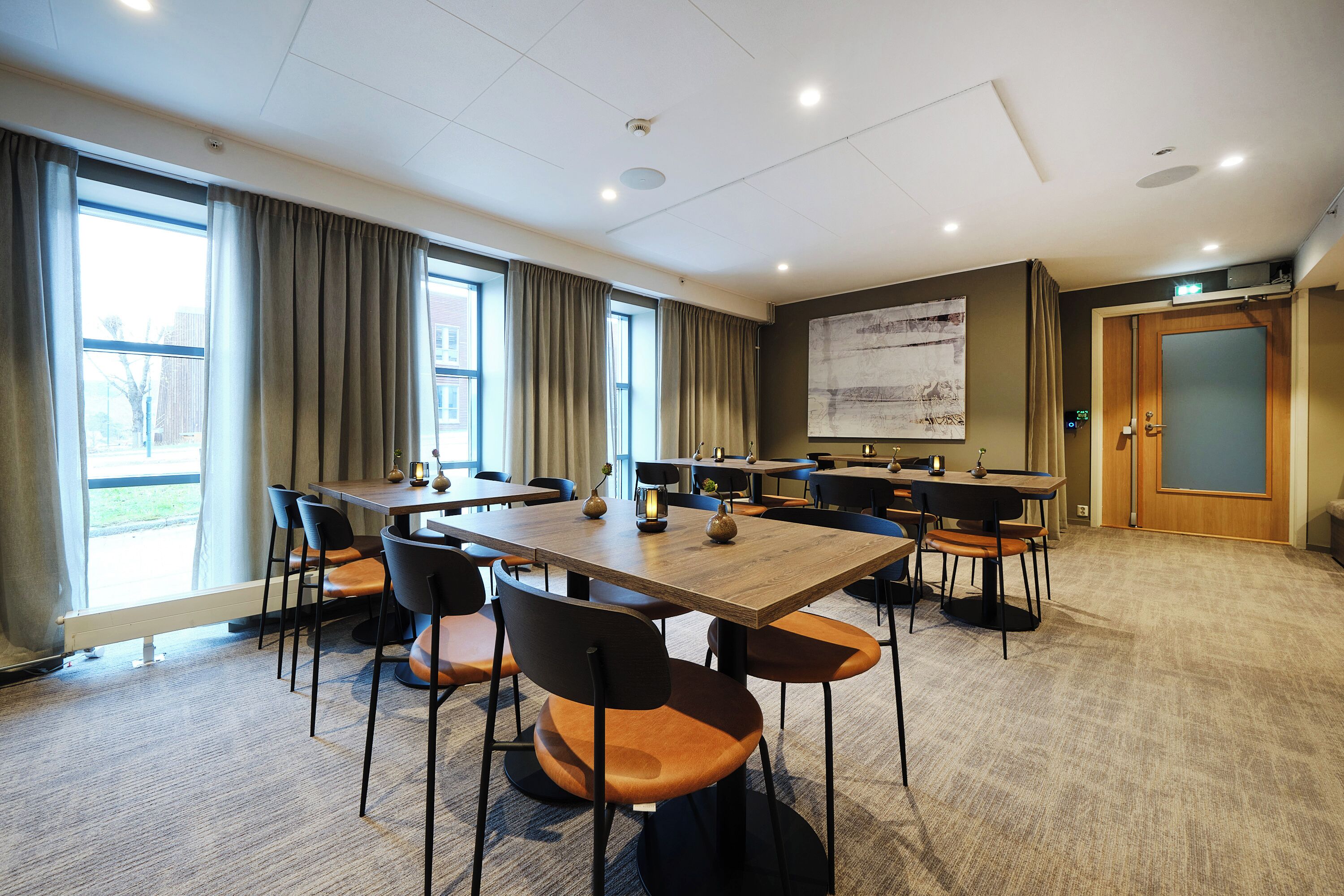 A conference room with tables and chairs, large windows, a projector screen, and a door.
