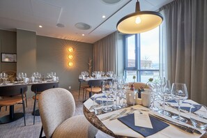 Een restaurantgedeelte in een hotel met gedekte tafels, stoelen en een groot raam met gordijnen.