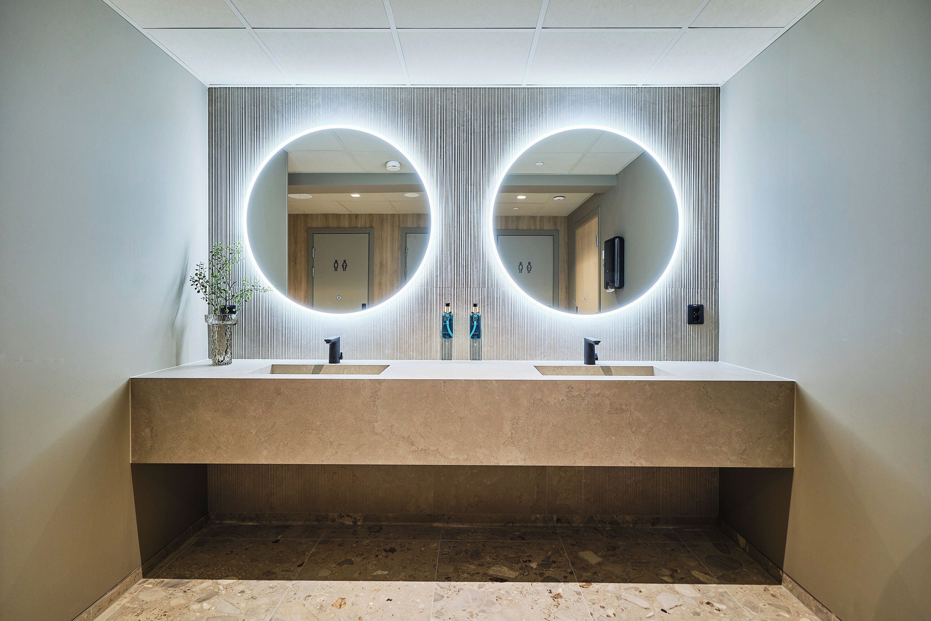 A modern bathroom with two sinks, a large mirror, and a potted plant.