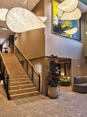 Een hotellobby met een trap, een grote potplant en een hedendaags kunstwerk.