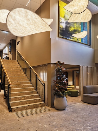 A hotel lobby with a staircase, a large potted plant, and a contemporary art piece.. Frich´s Hotel Surnadal