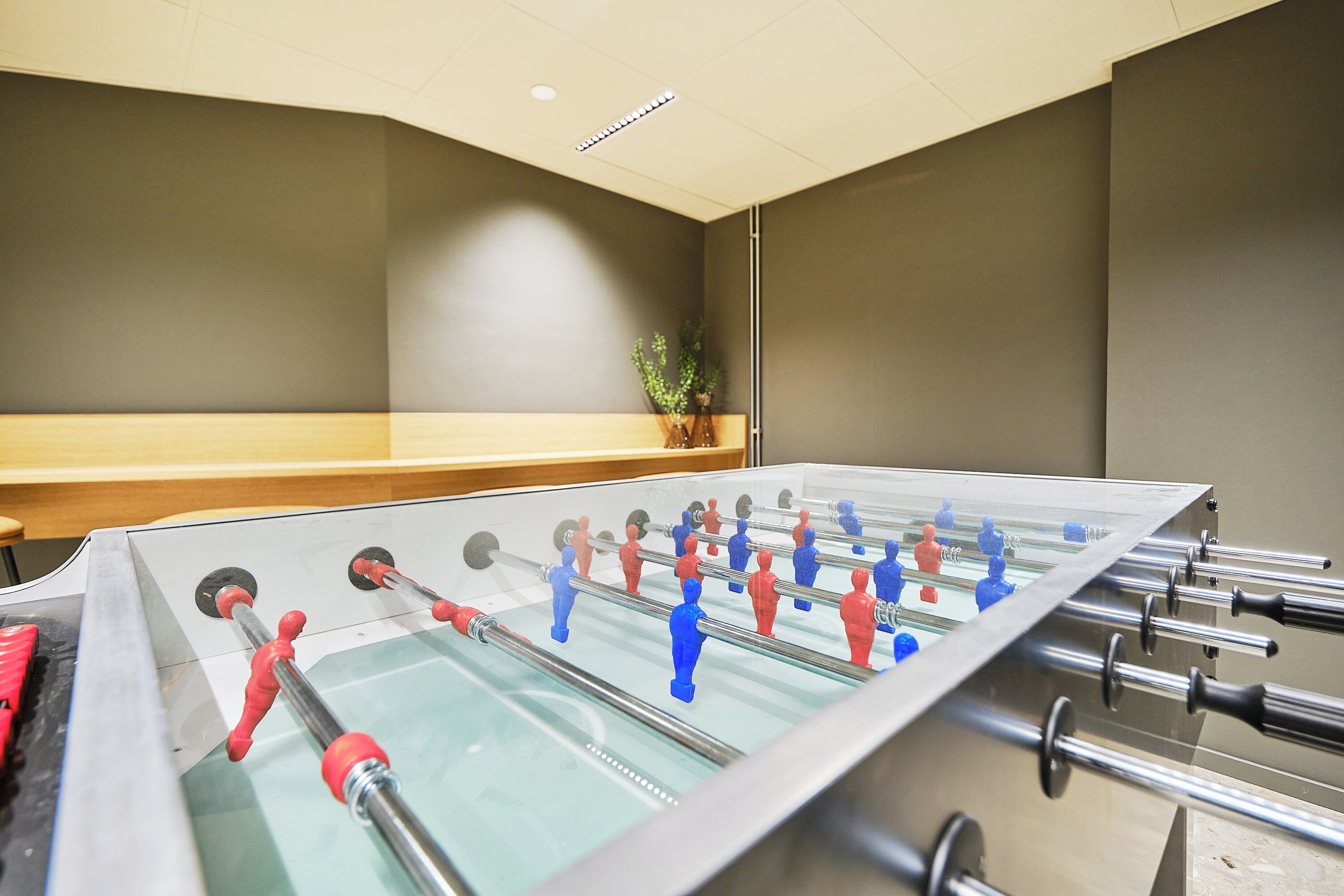 A foosball table in a room with a wooden bench and a potted plant.