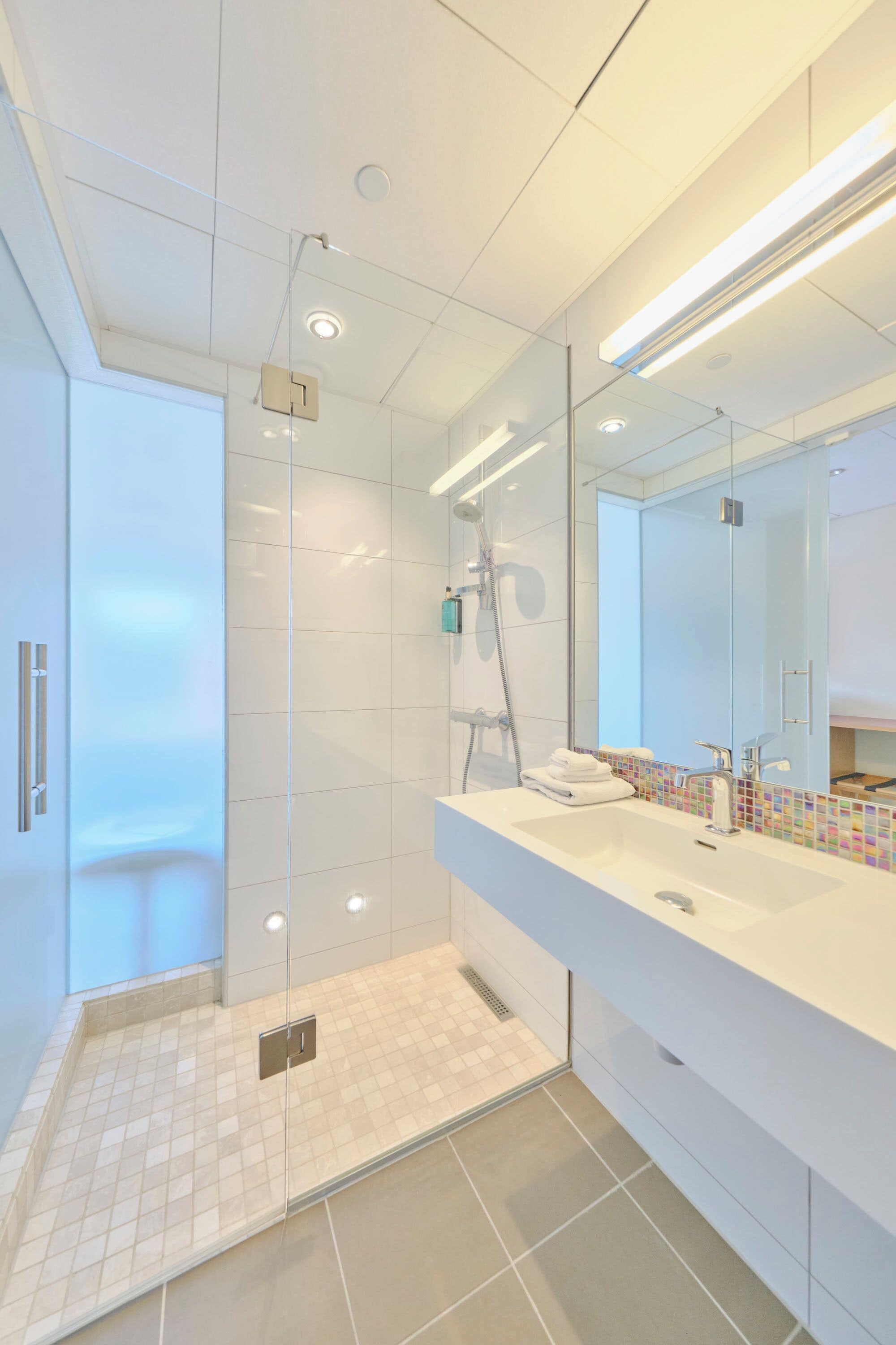 A modern bathroom with a glass shower enclosure, a white sink with a colorful mosaic backsplash, and a large mirror.