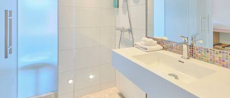 A modern bathroom with a glass shower enclosure, a white sink with a colorful mosaic backsplash, and a large mirror.