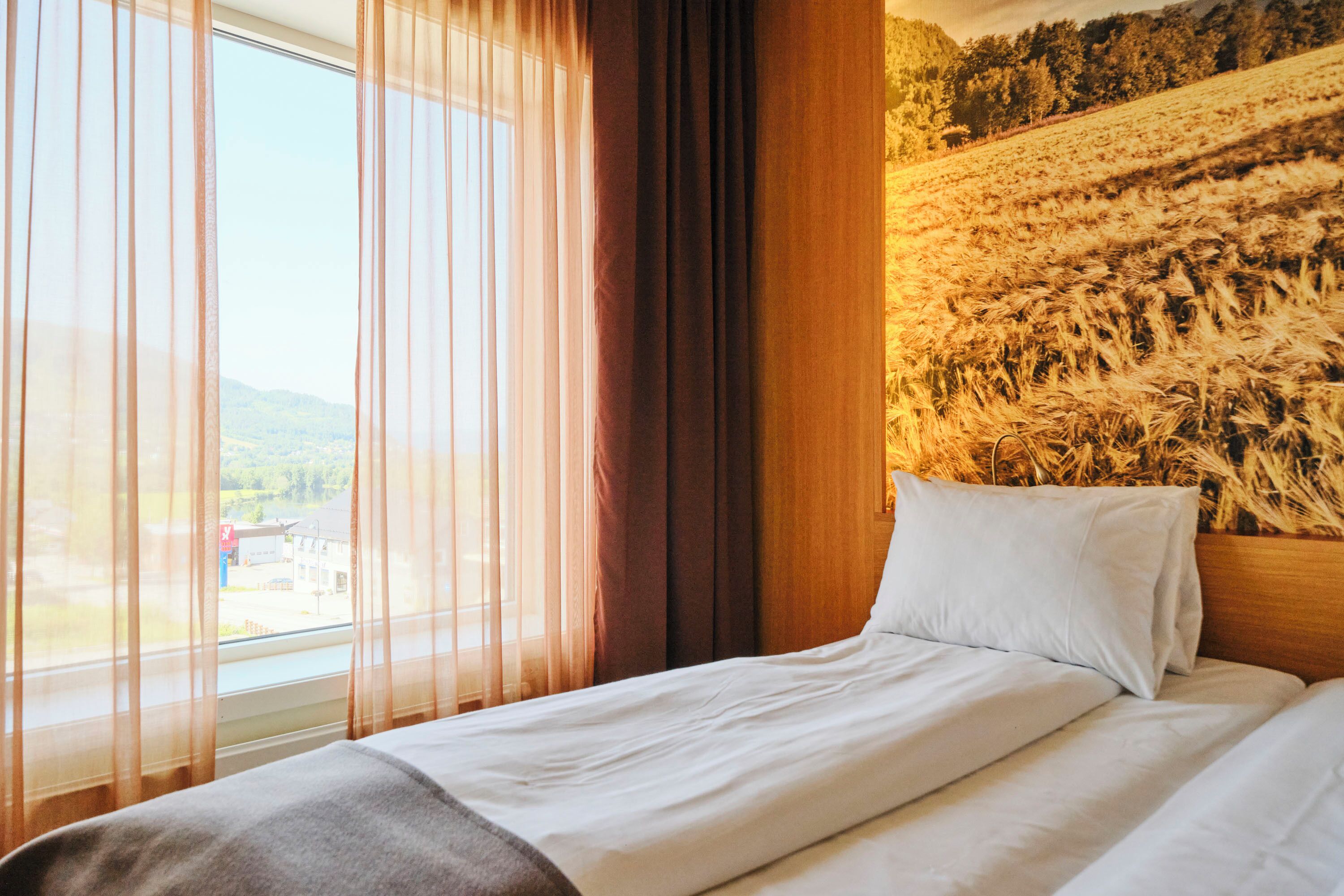 A hotel room with a bed, a window with sheer curtains, and a wall with a textured pattern.