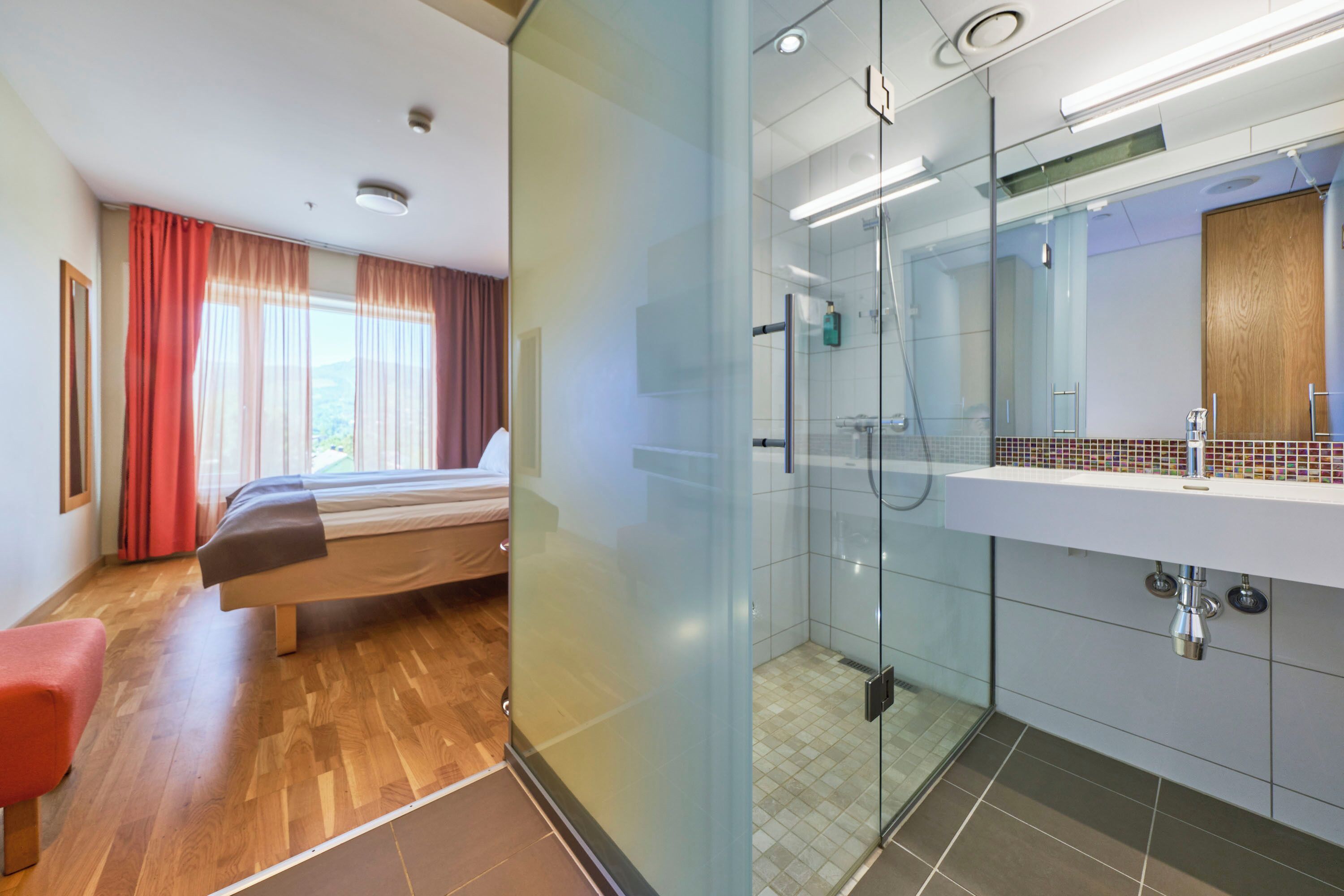 Une chambre d’hôtel comprenant un lit, une douche en verre, une salle de bain avec un miroir et un lavabo, et une vue sur l’extérieur par la fenêtre.
