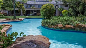 Una piscina de borde curvo, rodeada de rocas y follaje, con un edificio al fondo.