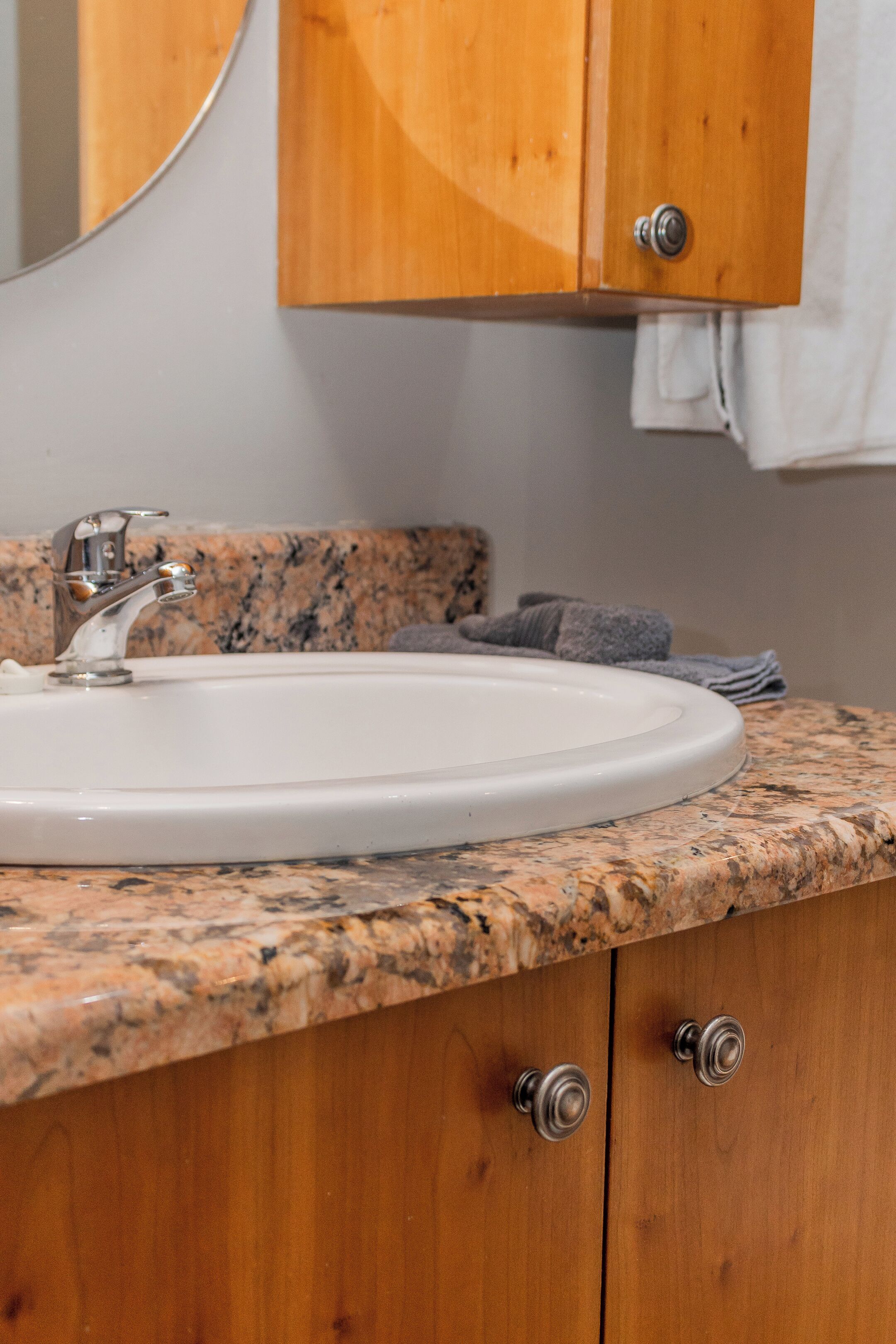 A bathroom with a granite countertop, a white sink, and wooden cabinets.