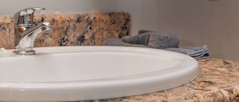 A bathroom with a granite countertop, a white sink, and wooden cabinets.