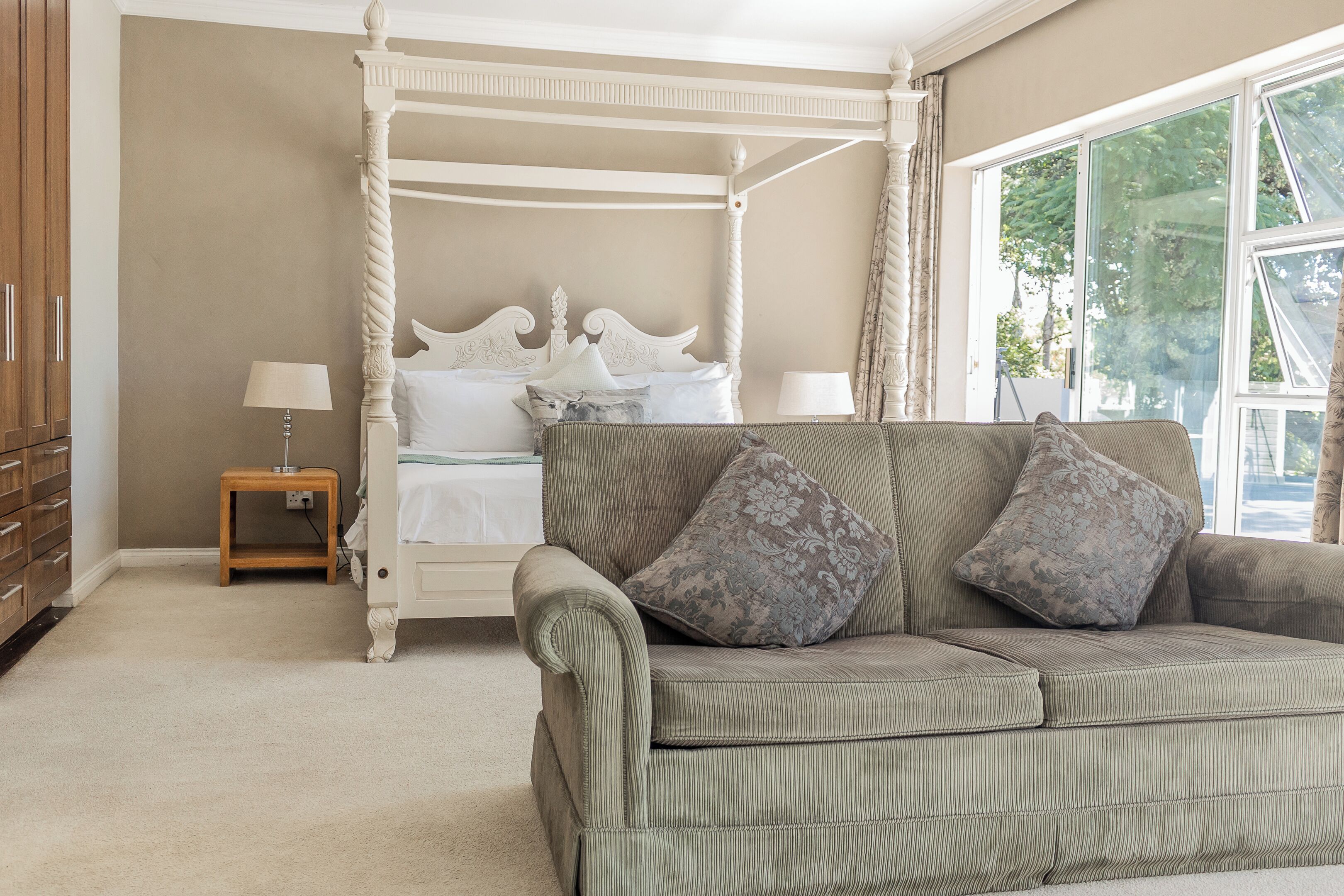 A bedroom with a four-poster bed, a green sofa, and a nightstand with a lamp.
