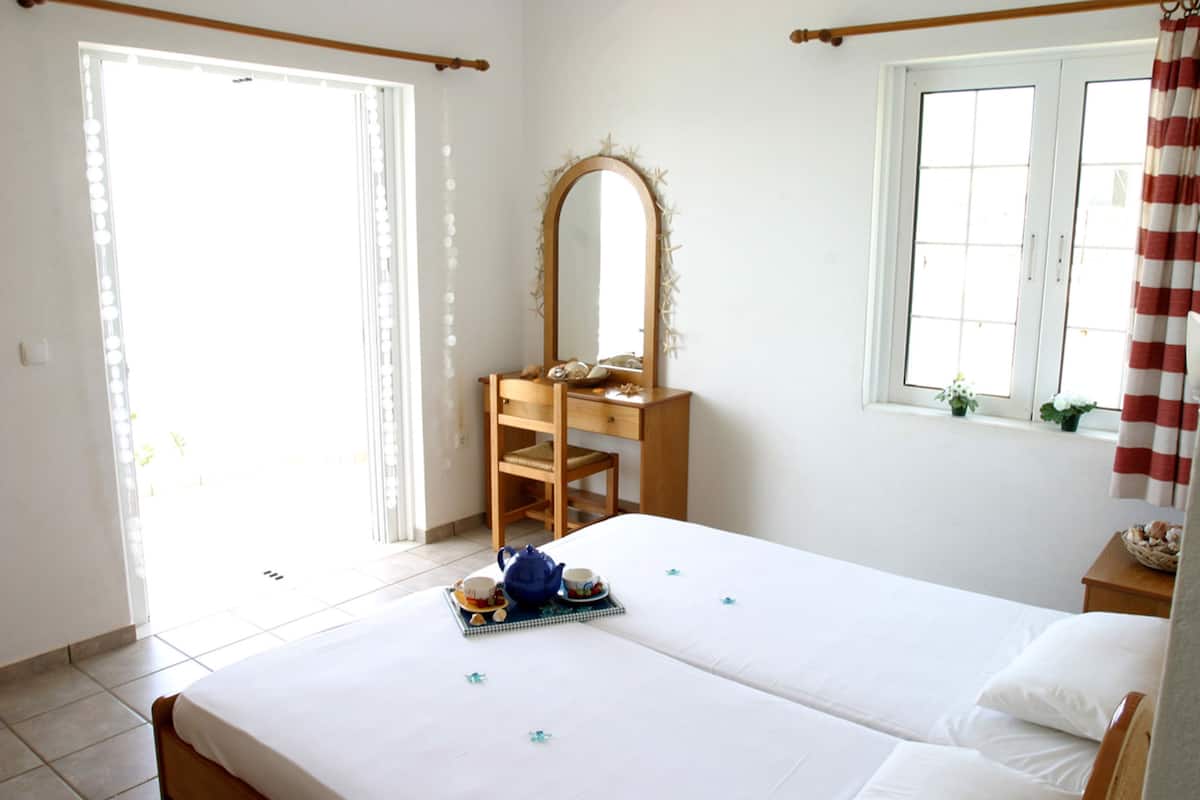 A hotel room with a bed, a wooden chair, a dresser, a mirror, and a window with curtains.