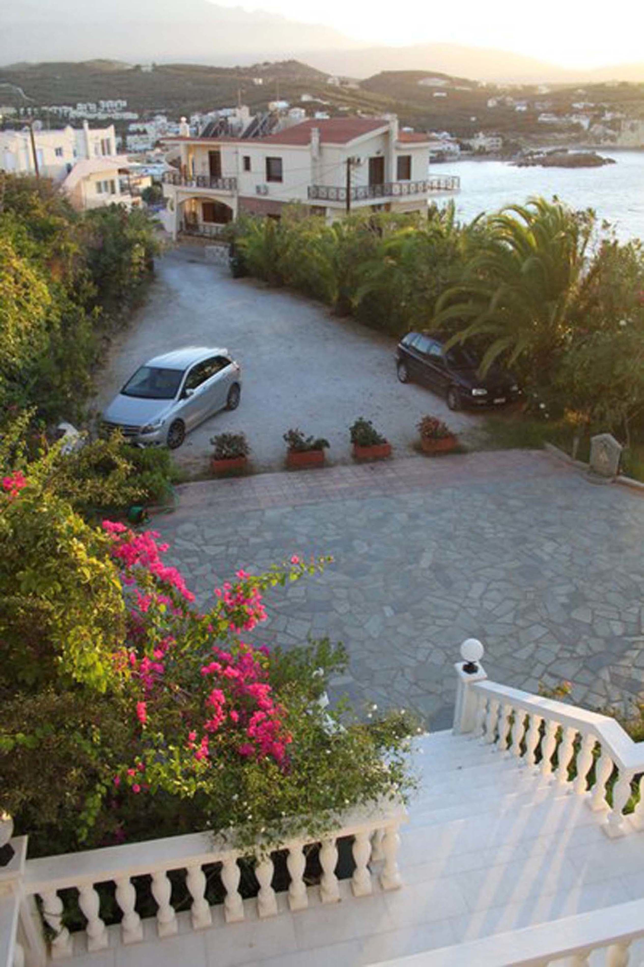 A residential area with a paved driveway, parked cars, and a staircase leading to a balcony.