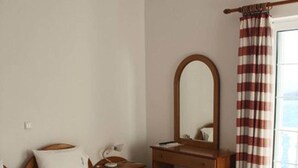 Une chambre d’hôtel avec un grand lit, une table de chevet en bois, un miroir et une fenêtre avec des rideaux à rayures.