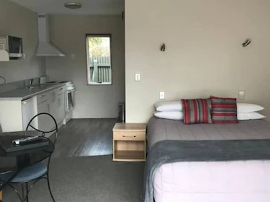 A compact room with a kitchenette, a bed with a striped pillow, and a desk with a chair.