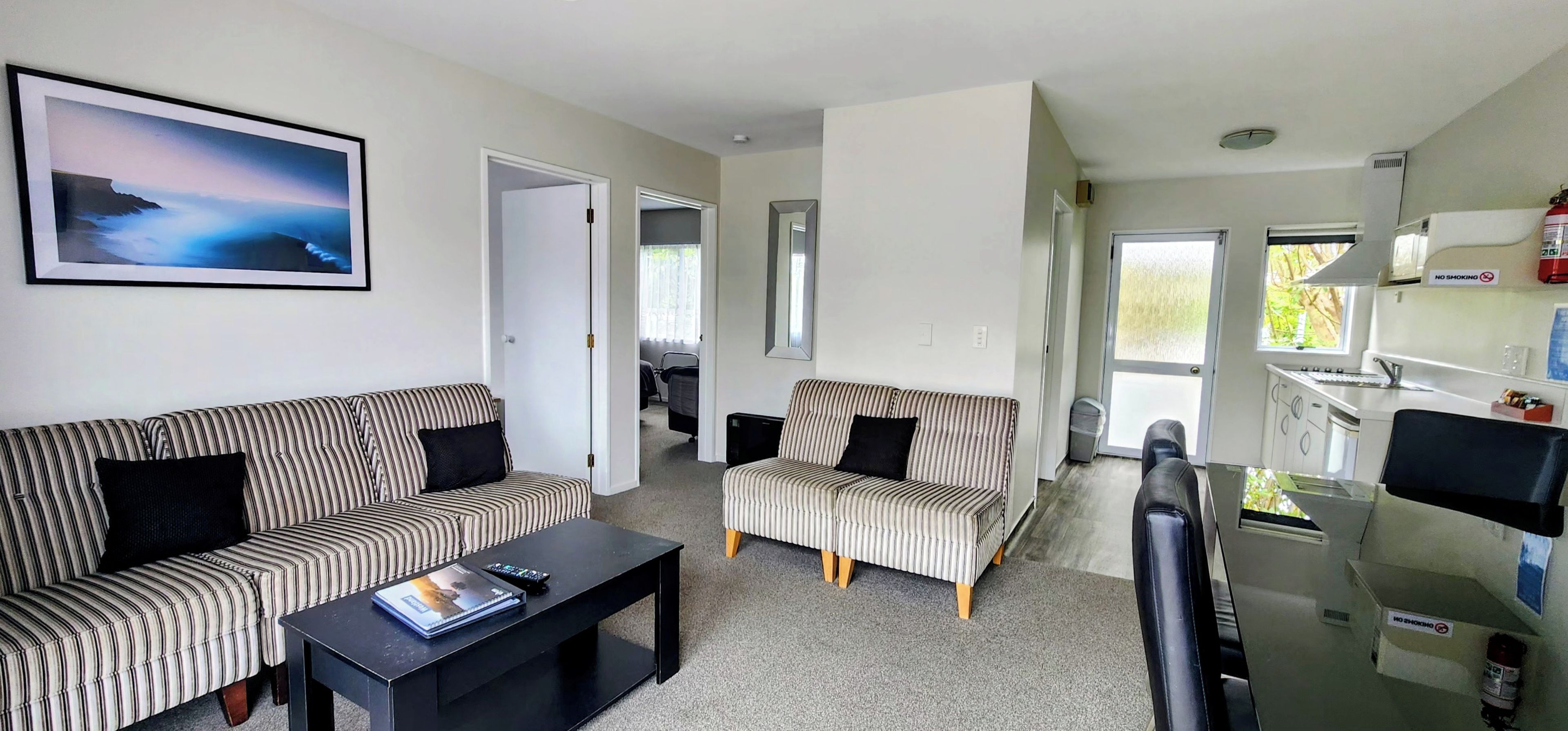 A living room with striped sofas, a coffee table, and a kitchen area with a sink and stove.