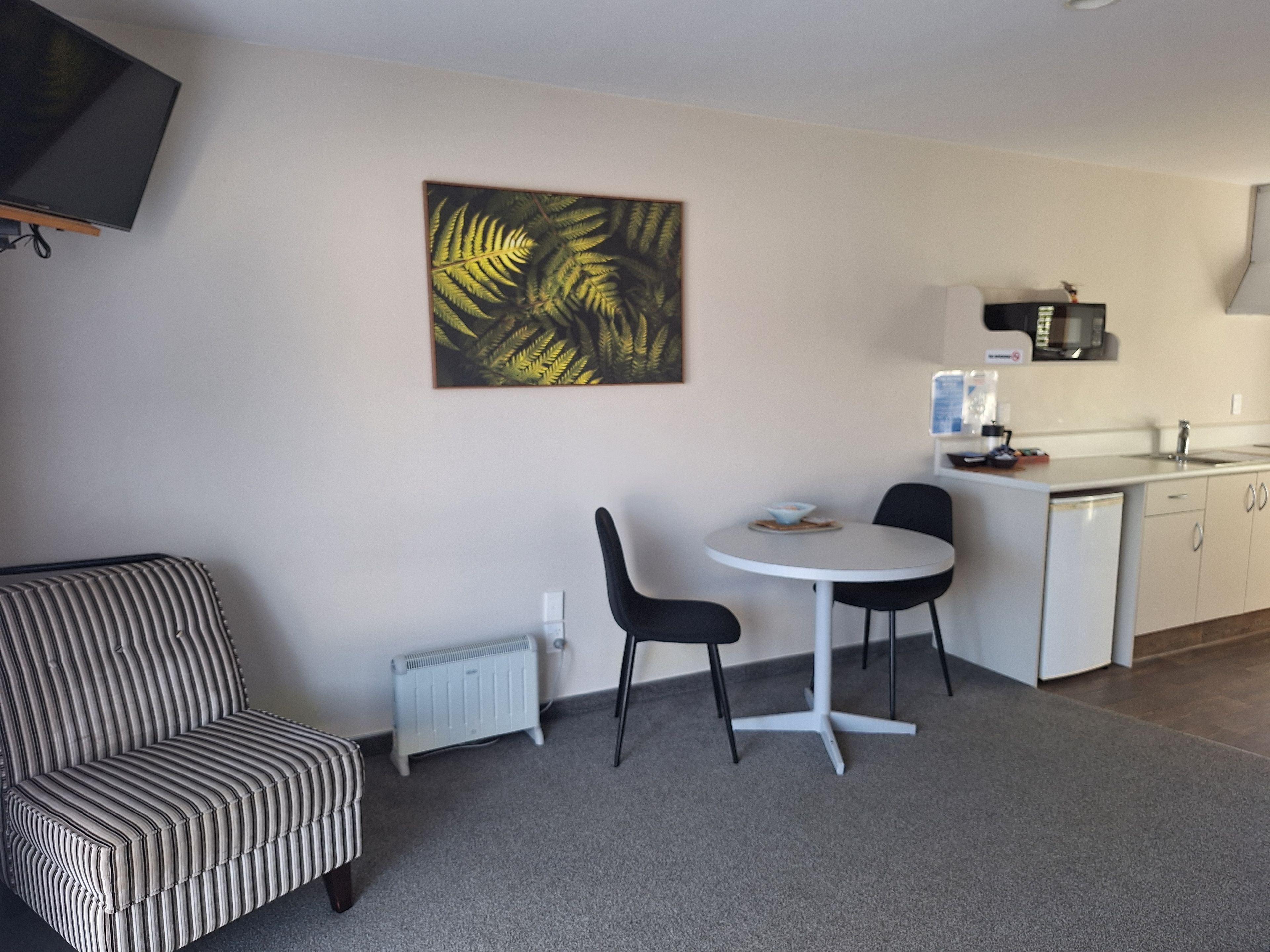 A compact living space with a kitchenette, a dining area with a table and chairs, a radiator, and a television mounted on the wall.