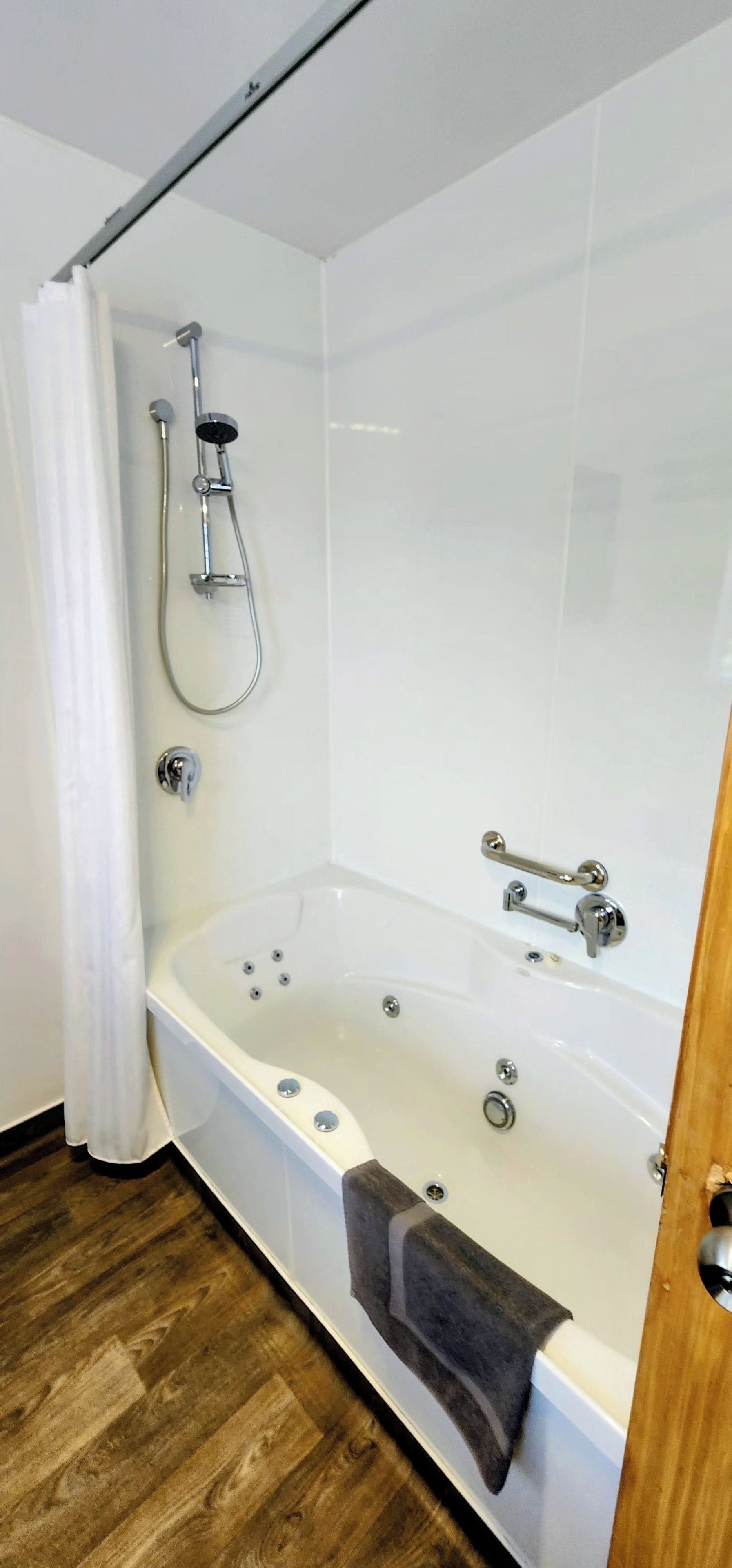 A bathroom with a bathtub, shower, and wooden flooring.