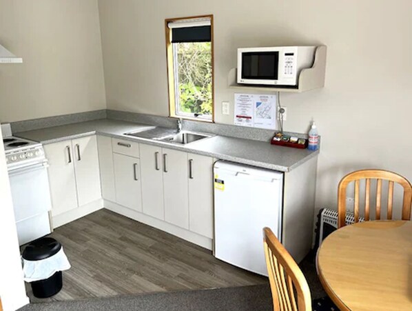 A compact kitchen with white cabinets, a microwave, a sink, and a small refrigerator. - Jade Court Motor Lodge (Hokitika)