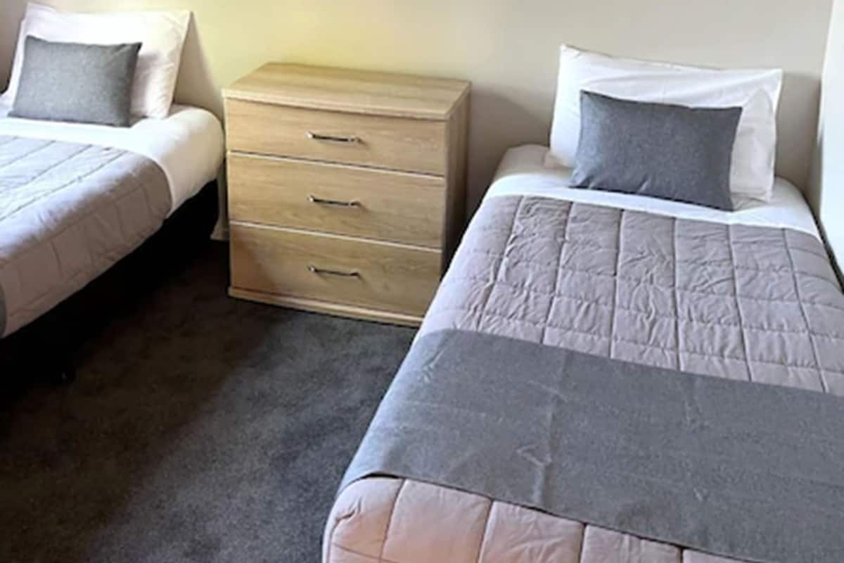 A bedroom with two single beds, a wooden dresser, and a mirror on the wall.