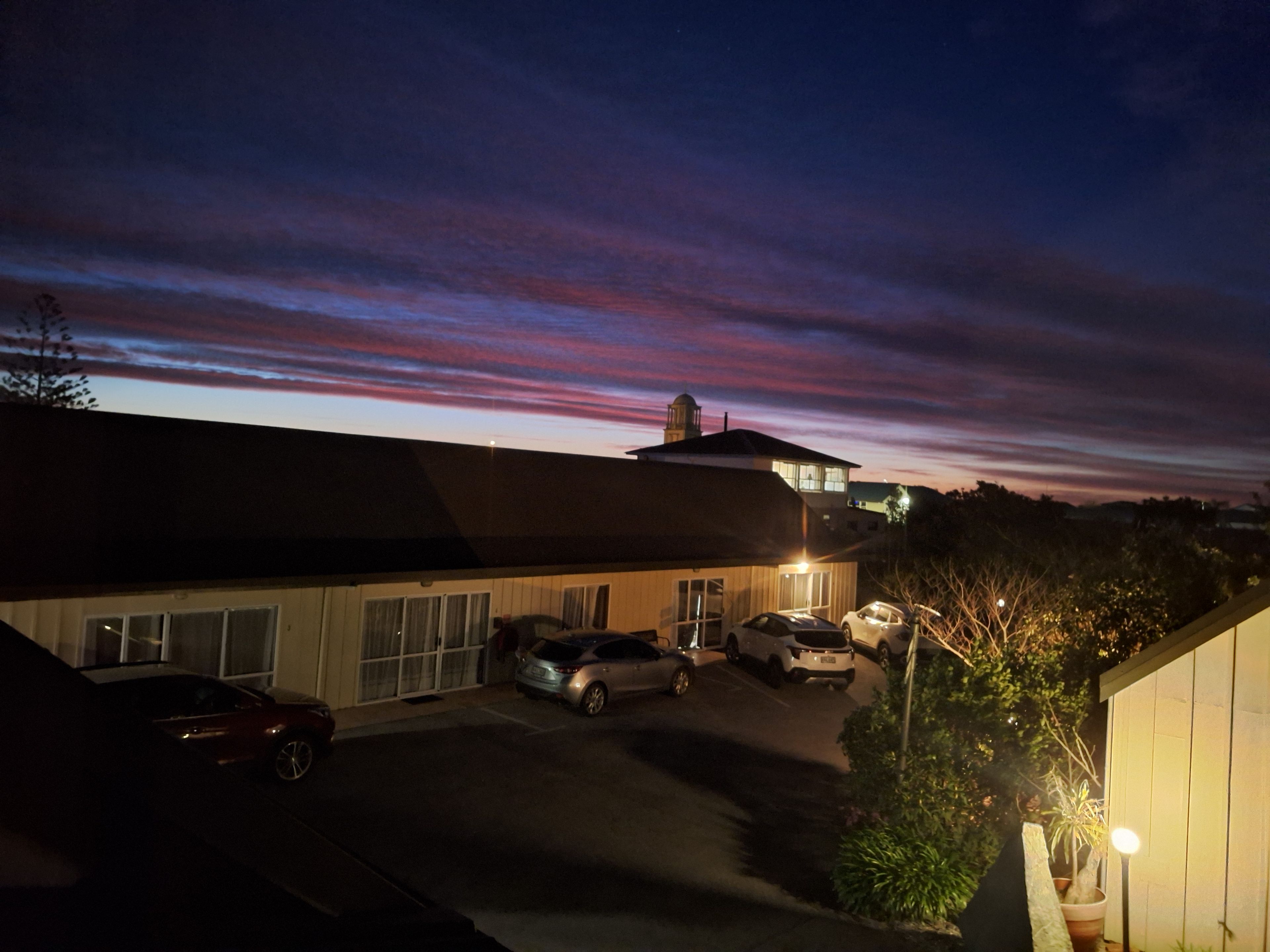 A residential area with a building, parked cars, and a clear sky.