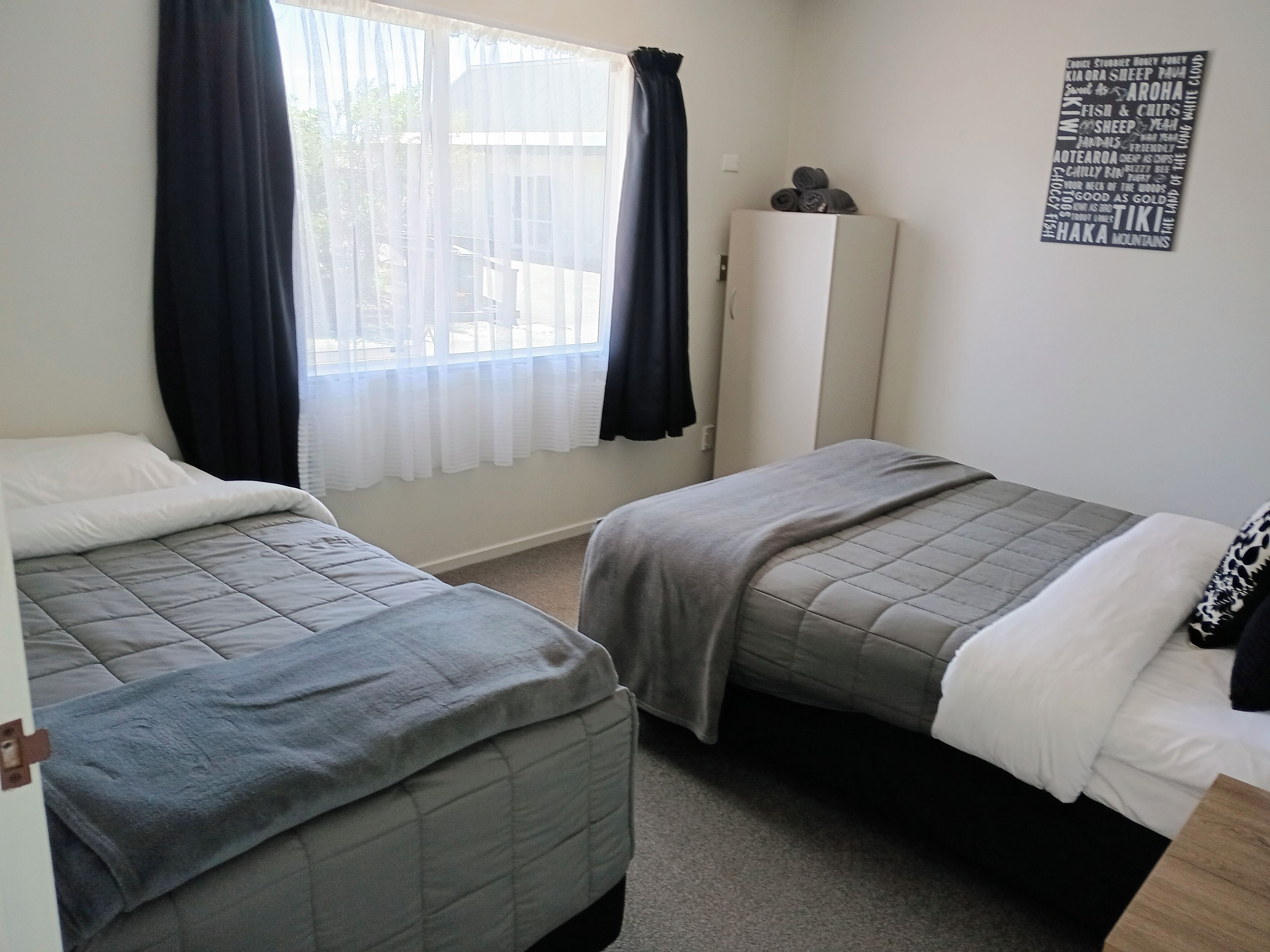 A bedroom with two beds, a window with curtains, a wardrobe, and a wall decoration.