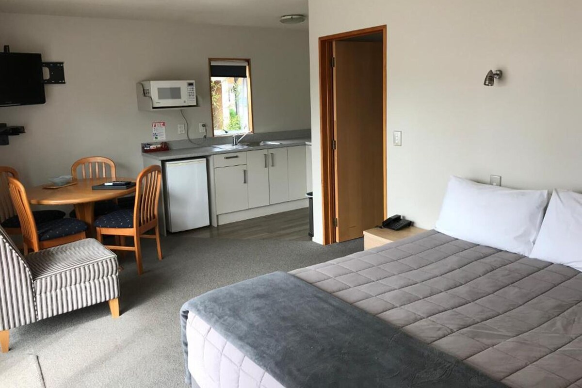A compact hotel room with a bed, a small kitchenette, a dining area, and a bathroom.