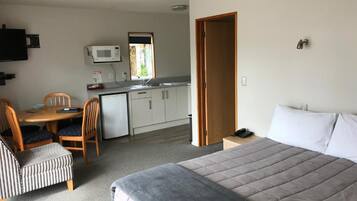 A compact hotel room with a bed, a small kitchenette, a dining area, and a bathroom.