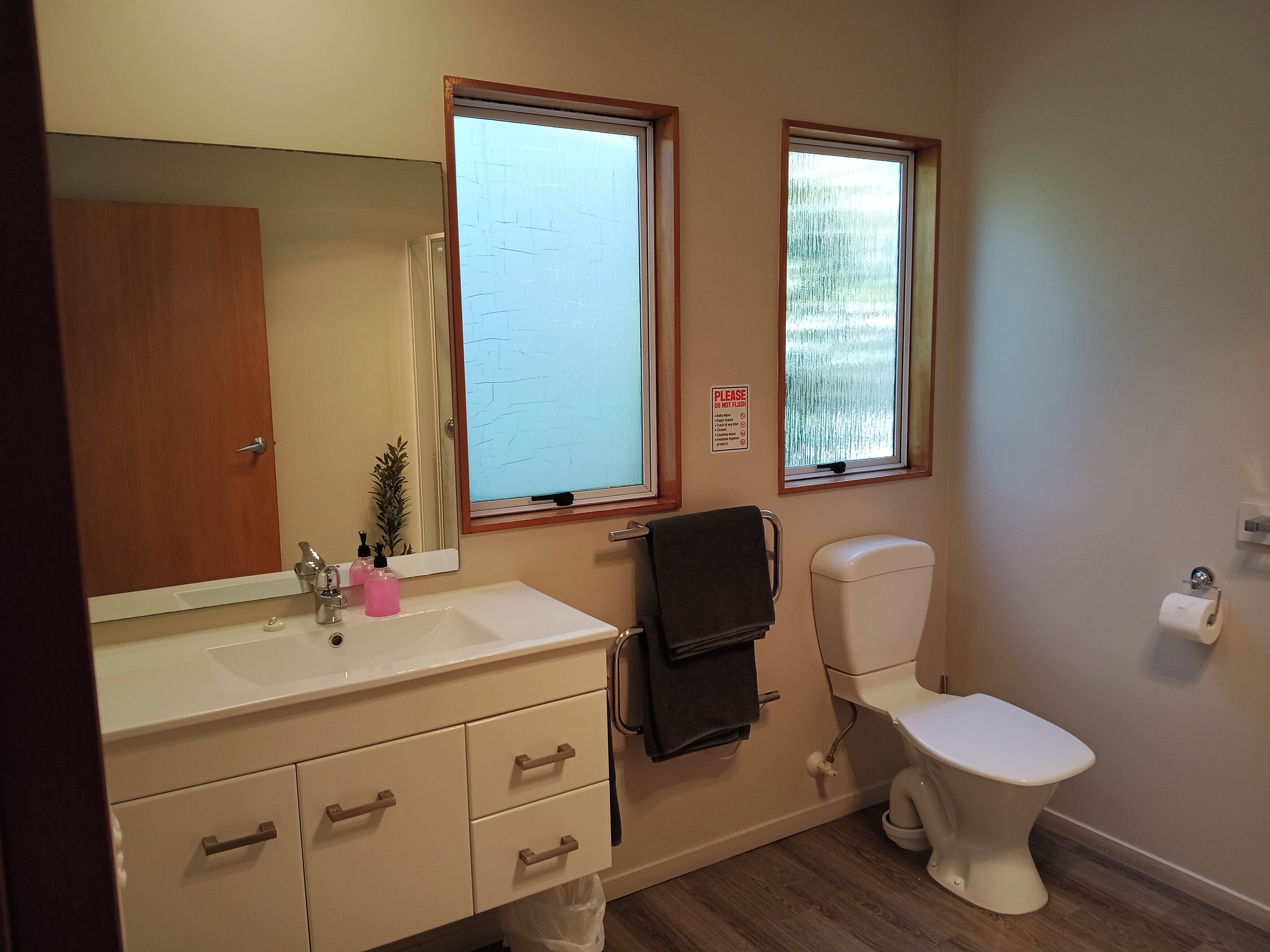 A bathroom with a white sink, a mirror, a toilet, and a window.
