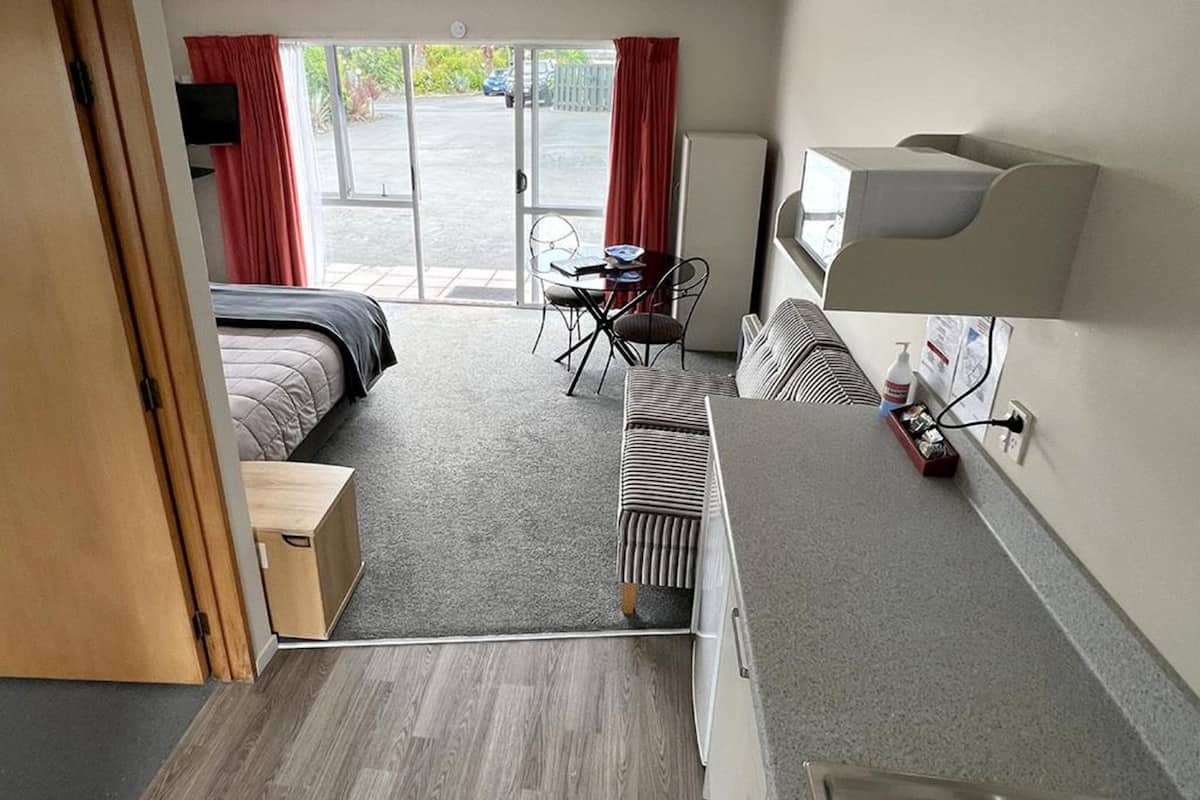 A hotel room with a bed, a desk, a chair, a radiator, a TV, and a window with curtains.