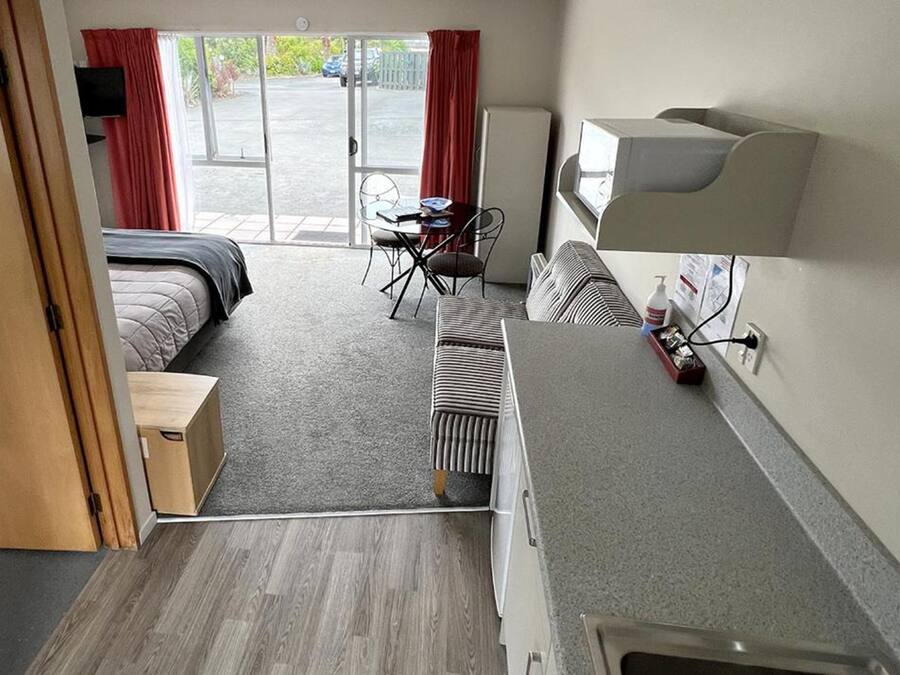 A hotel room with a bed, a desk, a chair, a radiator, a TV, and a window with curtains.