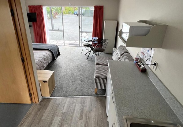 A hotel room with a bed, a desk, a chair, a radiator, a TV, and a window with curtains. - Jade Court Motor Lodge (Hokitika)
