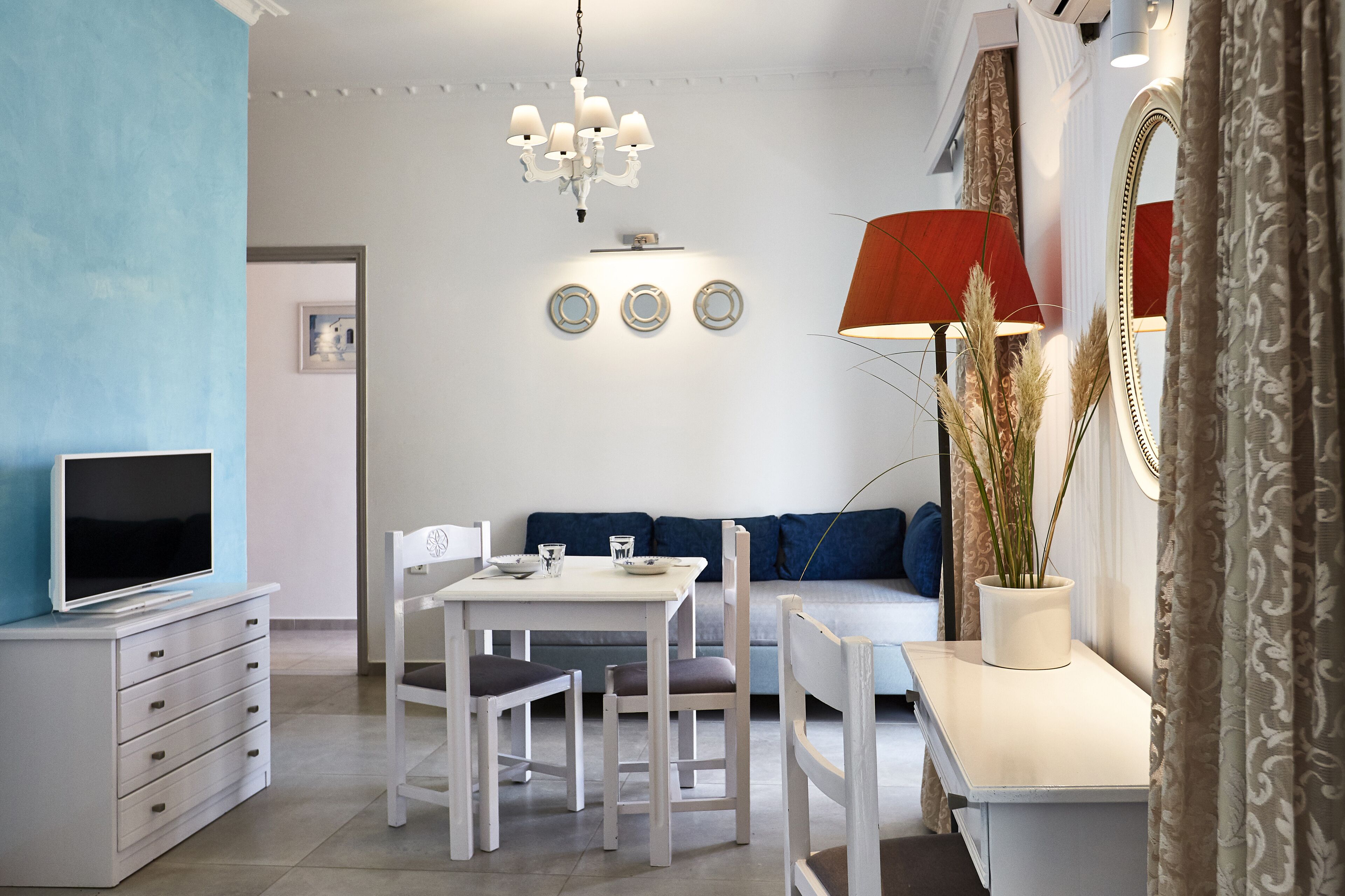 A modern living room with a dining area, a television, a chandelier, and a sofa.