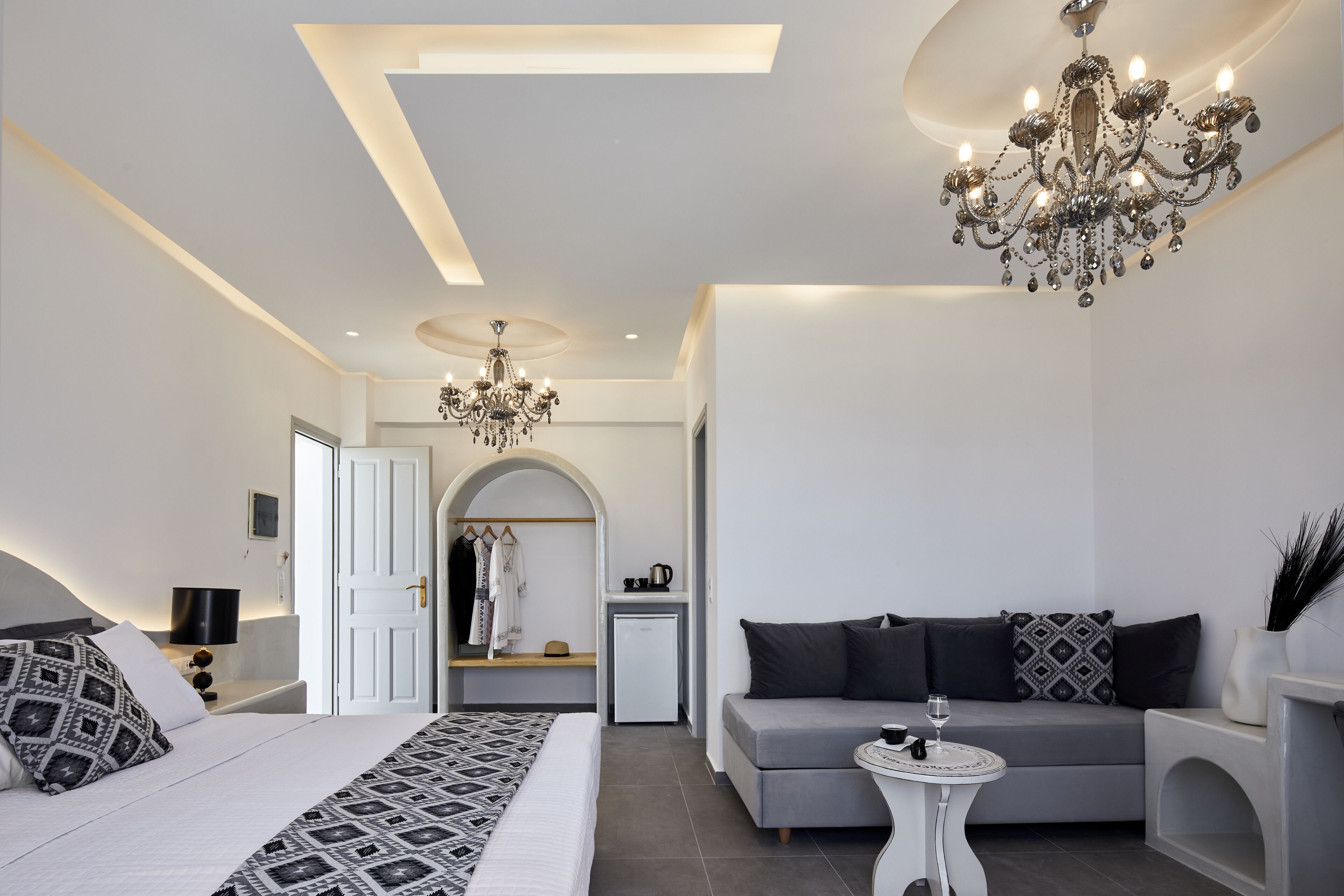 A modern bedroom with a large bed, a grey sofa, a small table, and a chandelier.