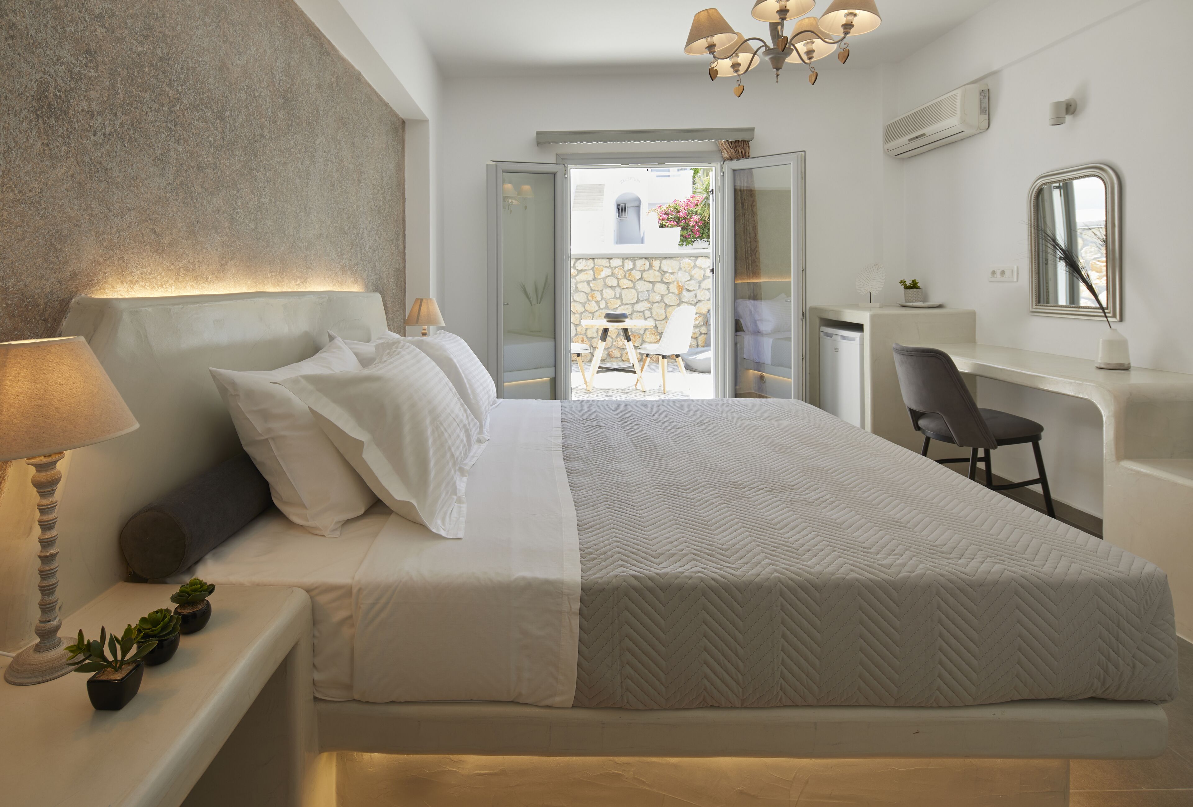 A modern bedroom with a large bed, bedside table with a lamp, and a view of an outdoor patio.