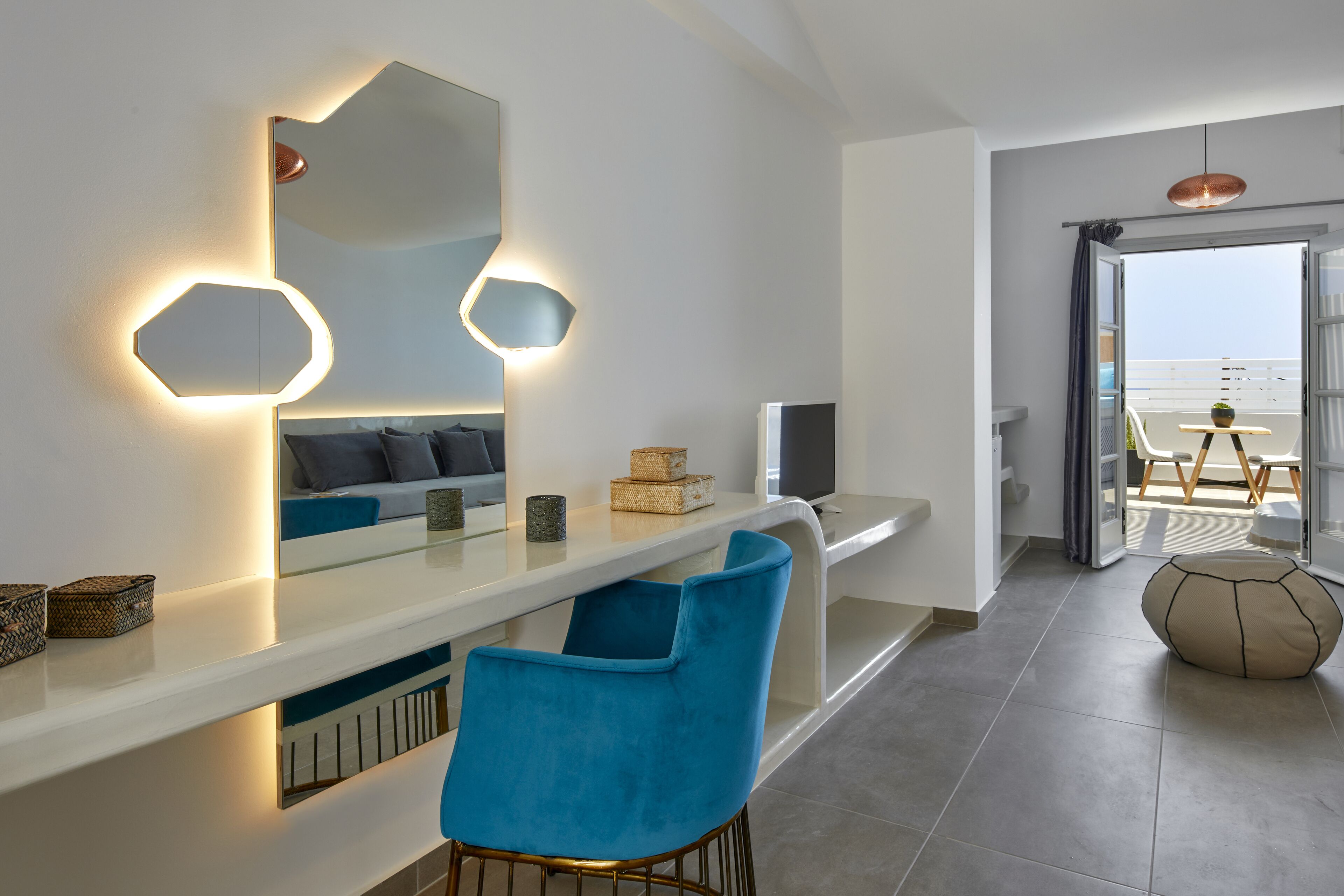 A modern living room with a white console table, blue chairs, a large mirror, and a view of the sea through an open door.