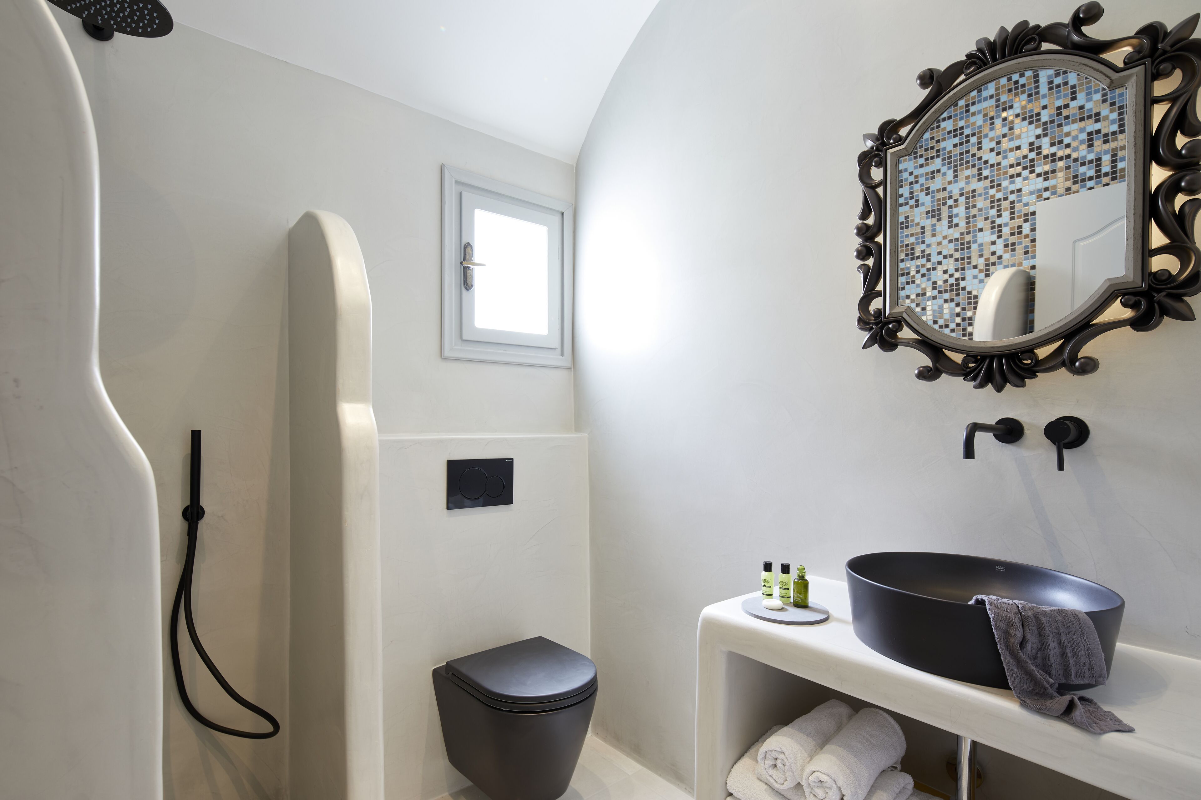 A modern bathroom with a black toilet, a white sink with a black basin, a mirror with a mosaic frame, and a shower area.