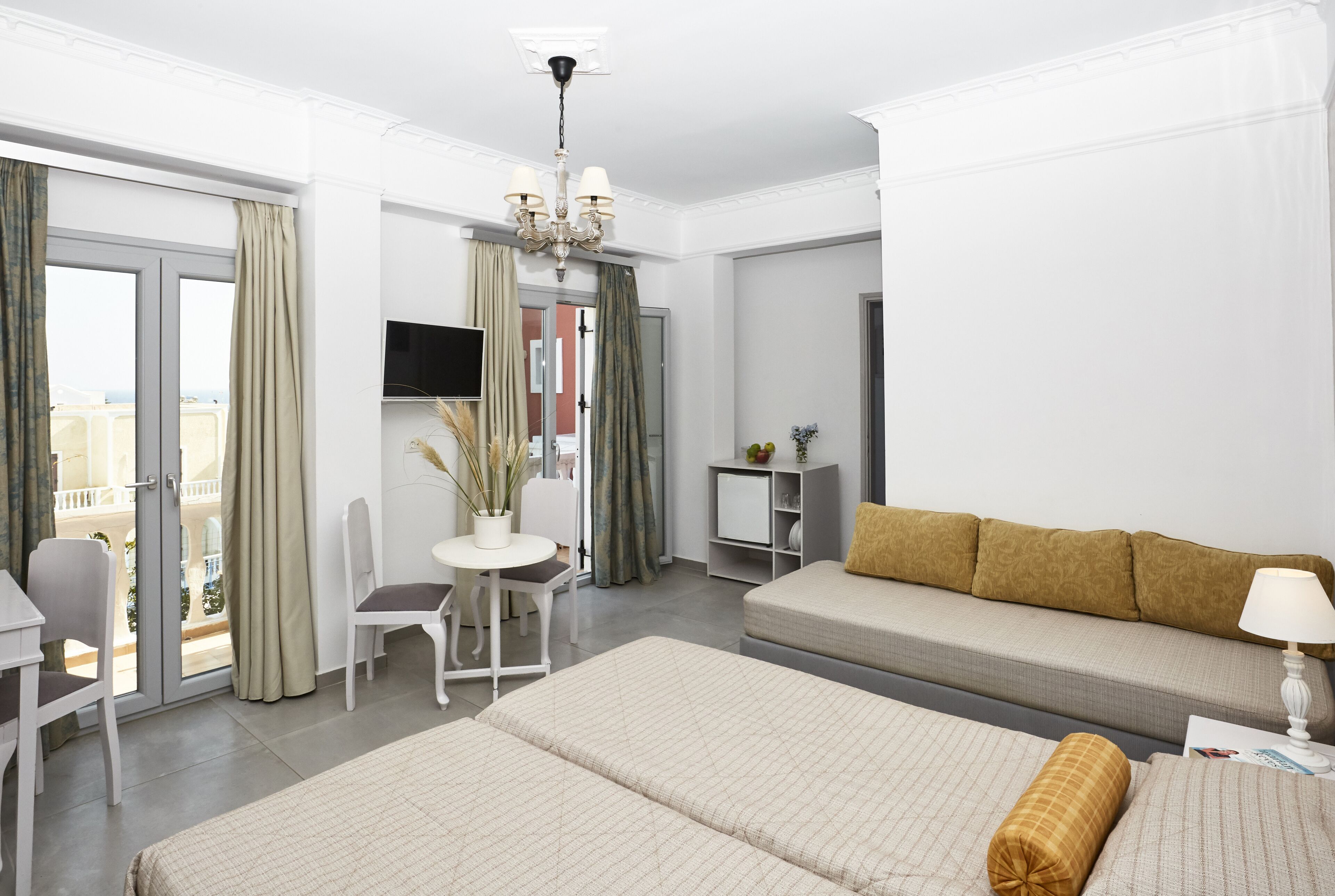 A hotel room with a bed, a sofa, a desk with a chair, a TV, and a balcony with curtains.