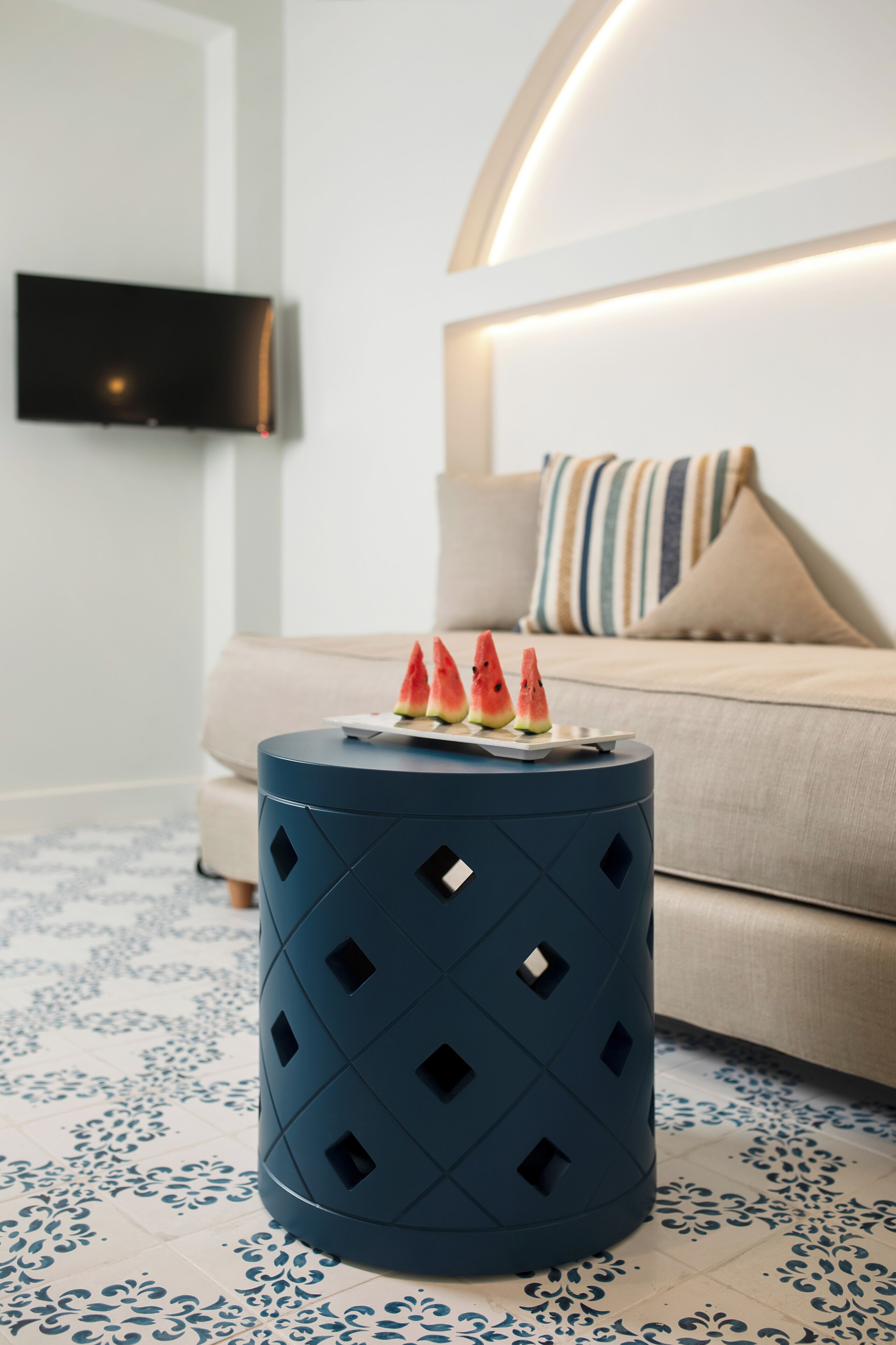 Una habitación moderna con un otoman azul redondo, un sofá, un televisor de pantalla plana y un cojín decorativo.