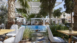 Un área de estar al aire libre con piso a cuadros, sillas blancas acolchadas y una piscina al fondo.