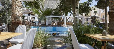 Un área de estar al aire libre con piso a cuadros, sillas blancas acolchadas y una piscina al fondo.