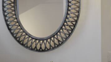 A wall-mounted mirror with a decorative metal frame, a light fixture, and three potted plants on a white console table.