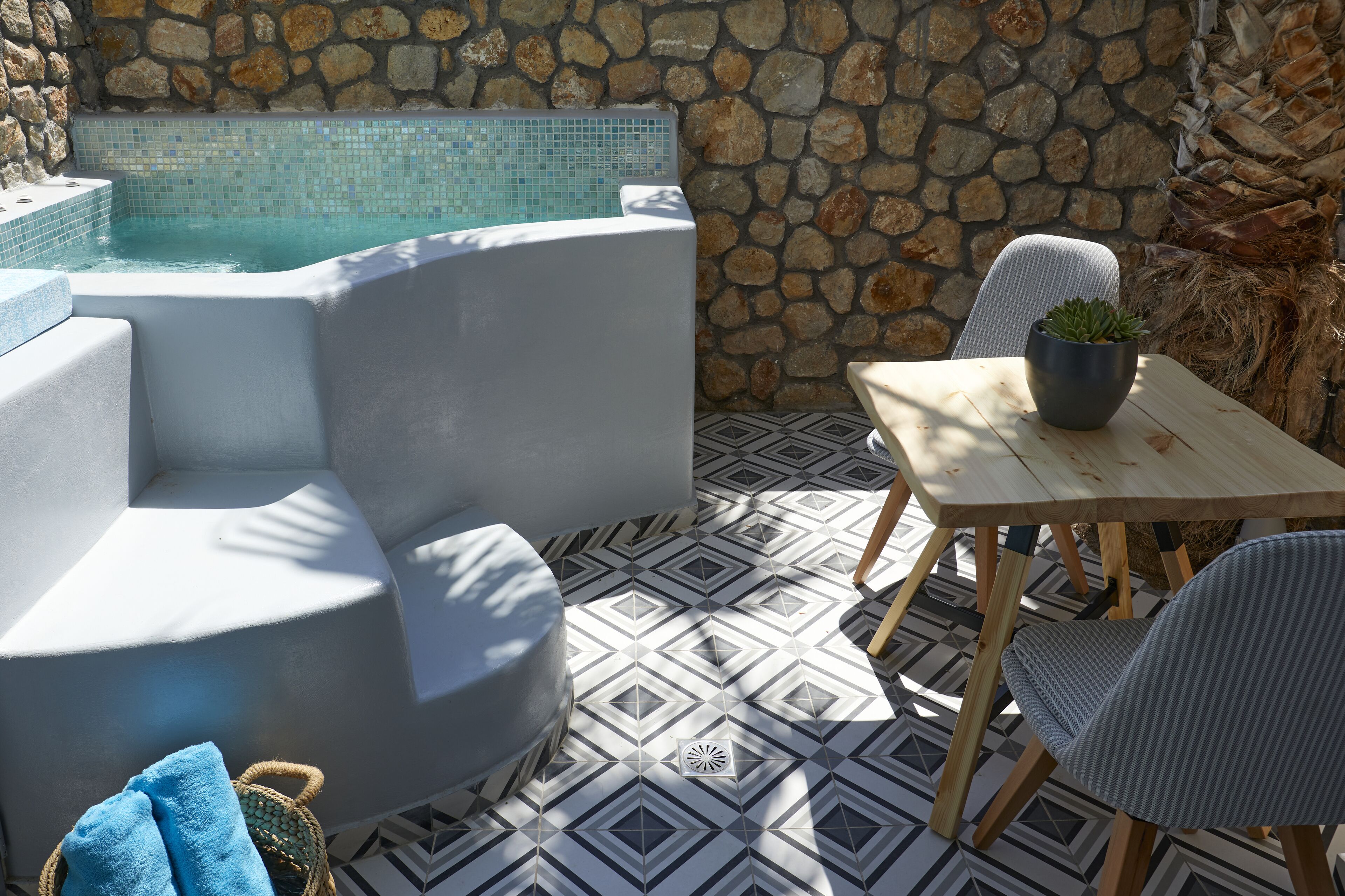 Ein moderner Außenbereich mit Sitzgelegenheit, einer Steinmauer, einem Pool und einem Tisch mit Stühlen.